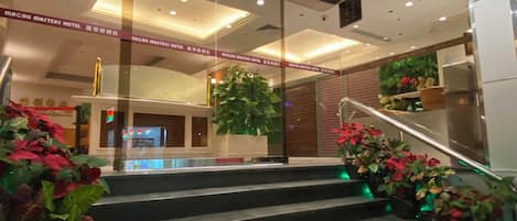 Entrada de un hotel con una escalera, puertas de cristal y plantas de interior.