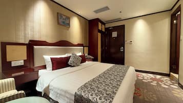 A hotel room with a large bed, a nightstand, a desk, a chair, and a door.