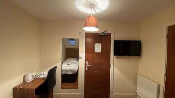A hotel room with two beds, a desk with a chair, a ceiling light, a TV mounted on the wall, and a door with a mirror.
