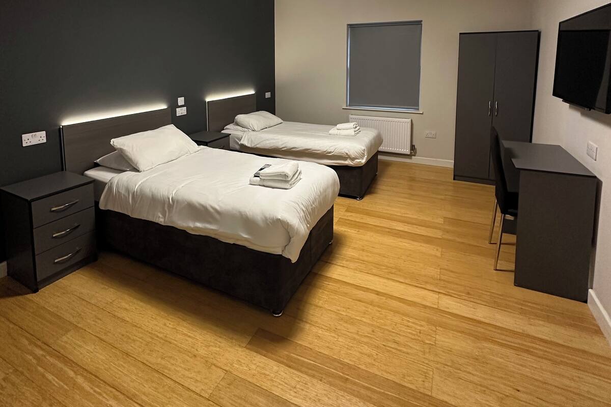 A modern bedroom with two beds, a desk, and a TV.