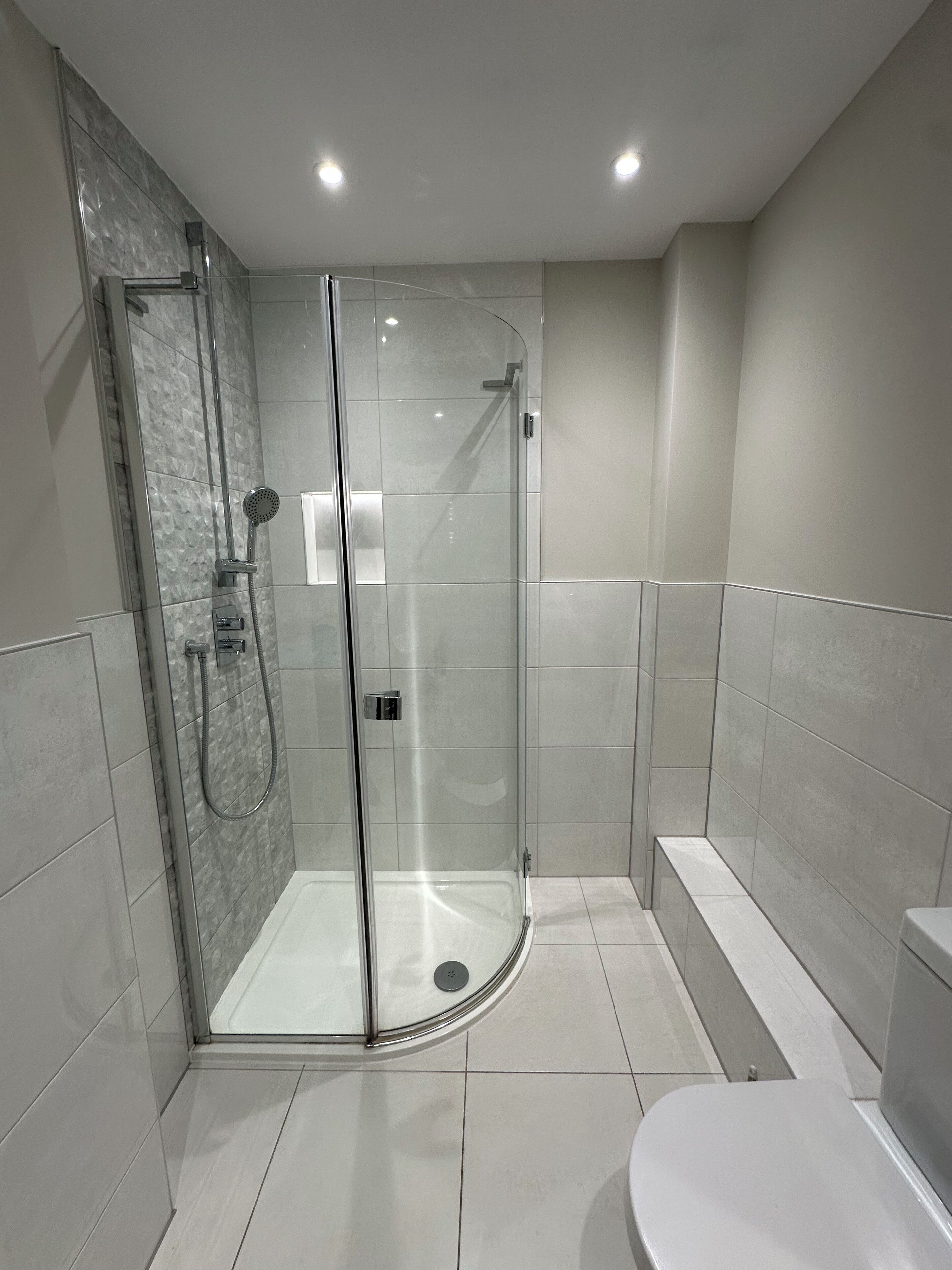 A modern bathroom with a glass-enclosed shower, a white toilet, and a bench.