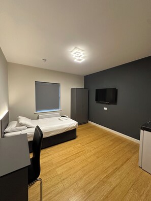 Een moderne slaapkamer met een bed, een bureau, een stoel, een kledingkast en een televisie aan de muur.