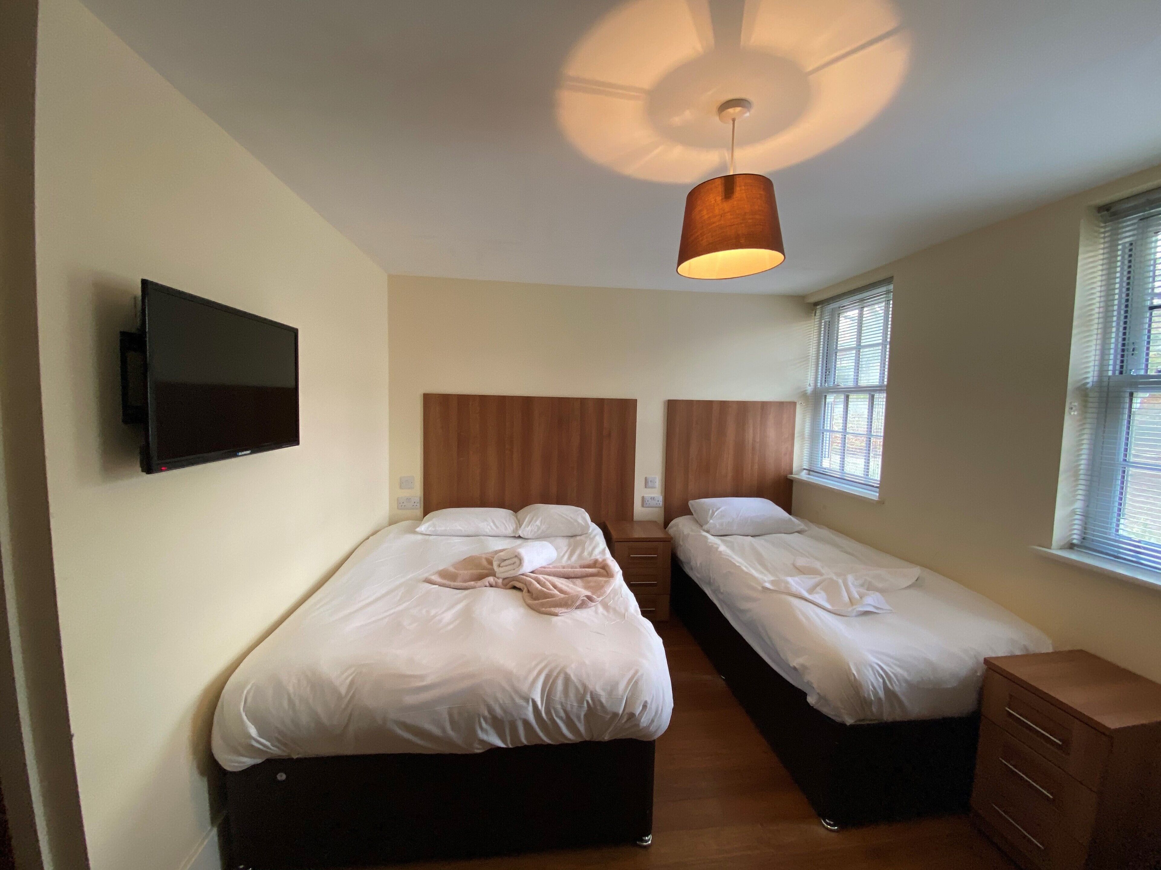A bedroom with two beds, a TV mounted on the wall, and a ceiling light fixture.