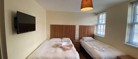A bedroom with two beds, a TV mounted on the wall, and a ceiling light fixture.