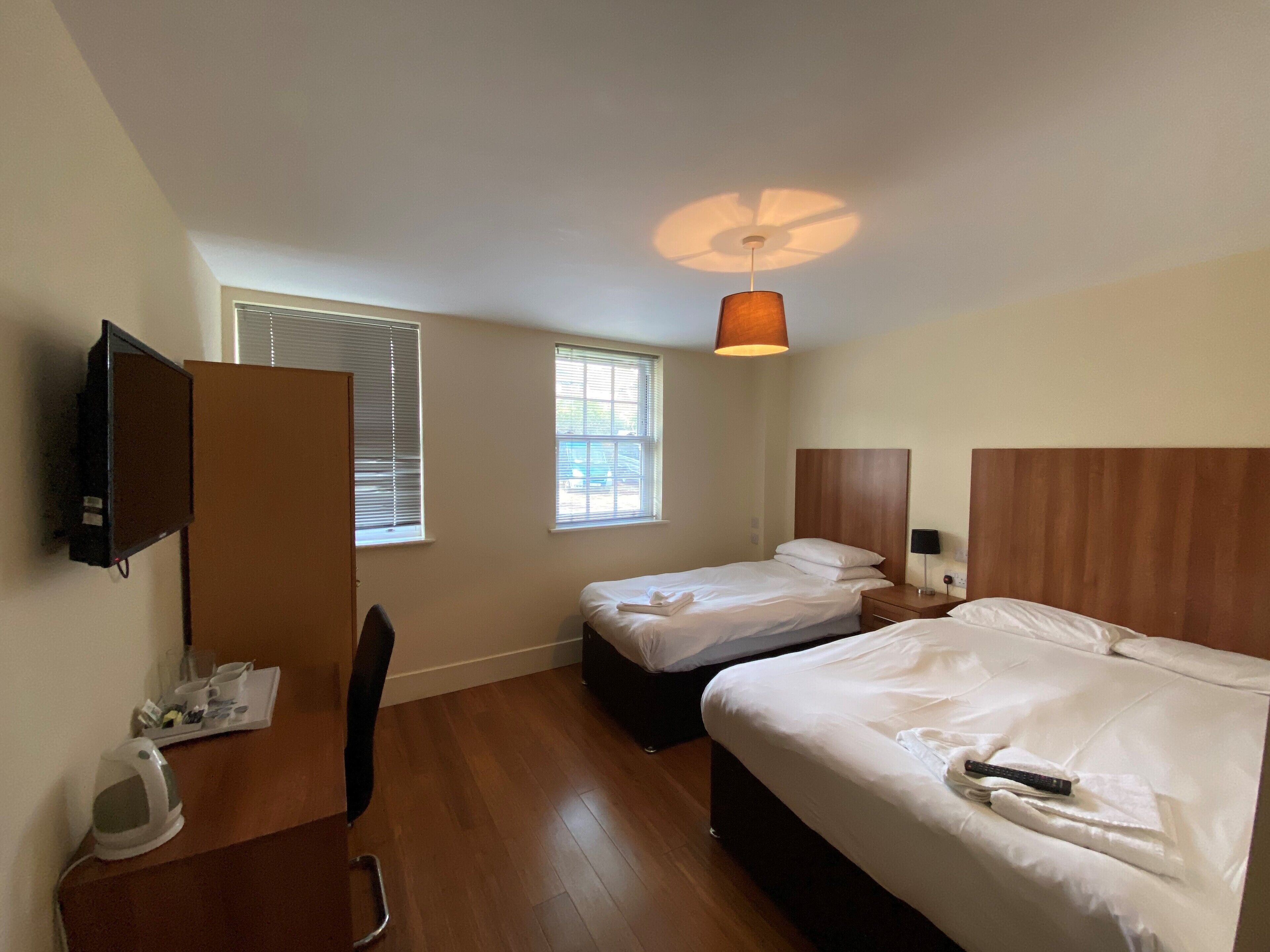 A hotel room with two beds, a TV, a desk with a chair, and a window with blinds.