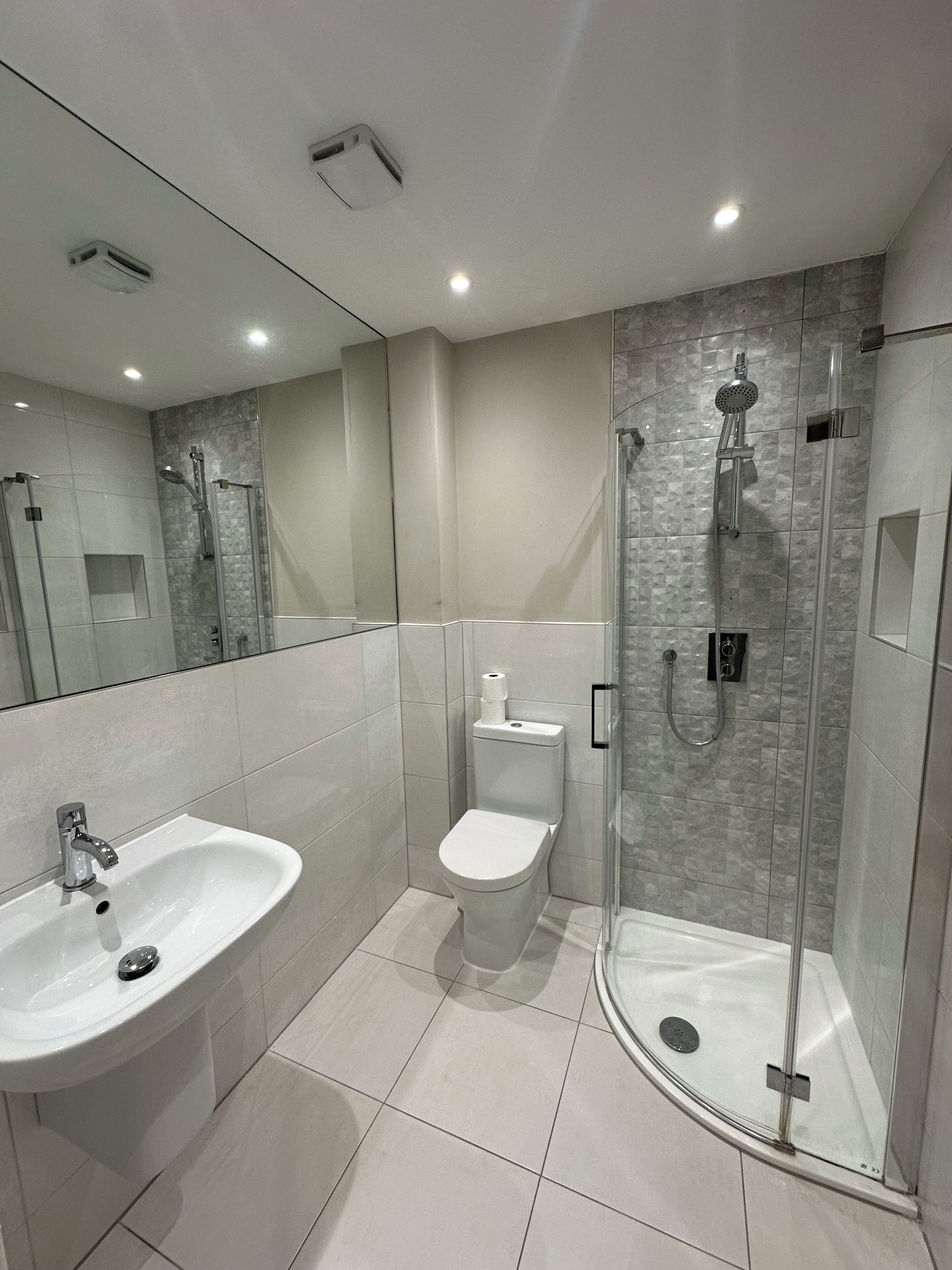 Un baño moderno con cabina de ducha de vidrio, un lavabo blanco y un inodoro.