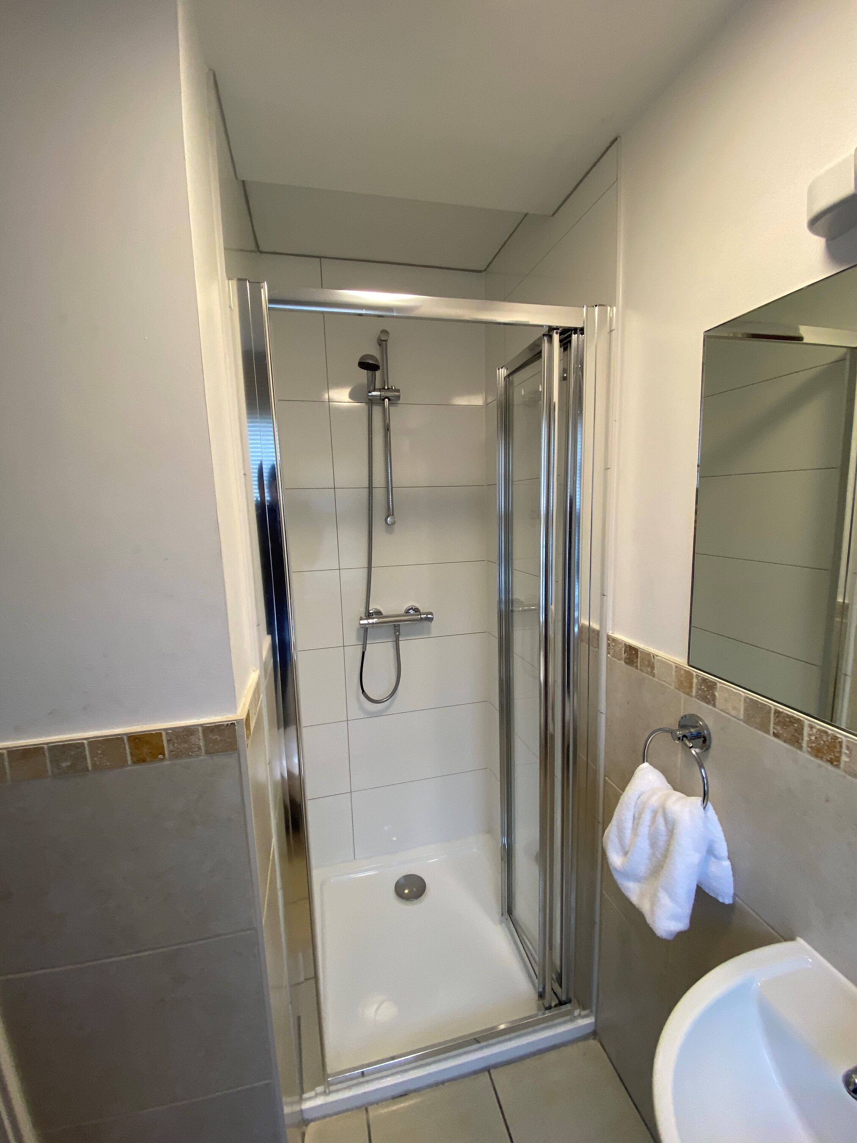 A glass-enclosed shower with a handheld showerhead and a wall-mounted faucet.