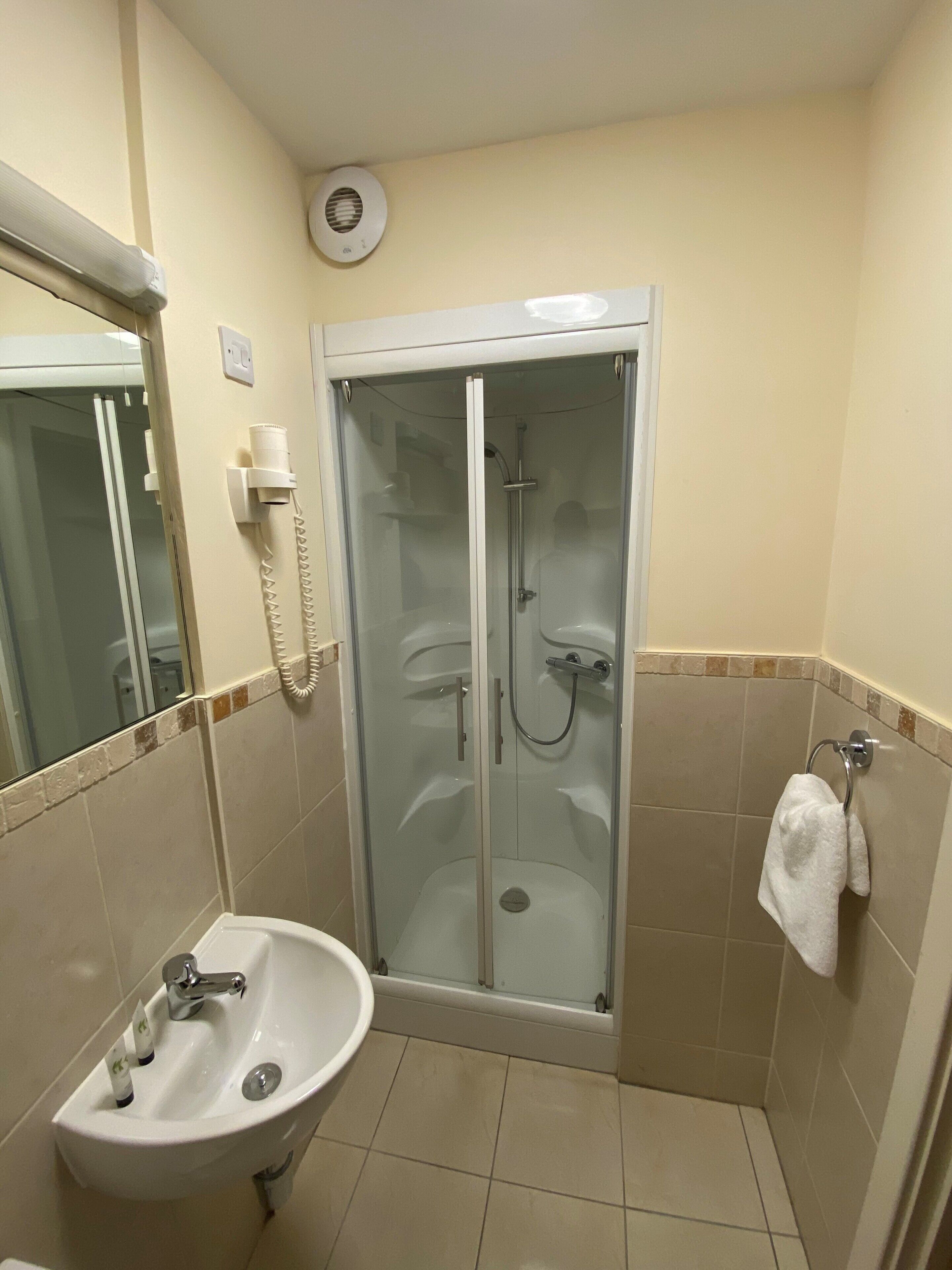 A bathroom with a glass-enclosed shower, a sink with a mirror, and a towel rack.