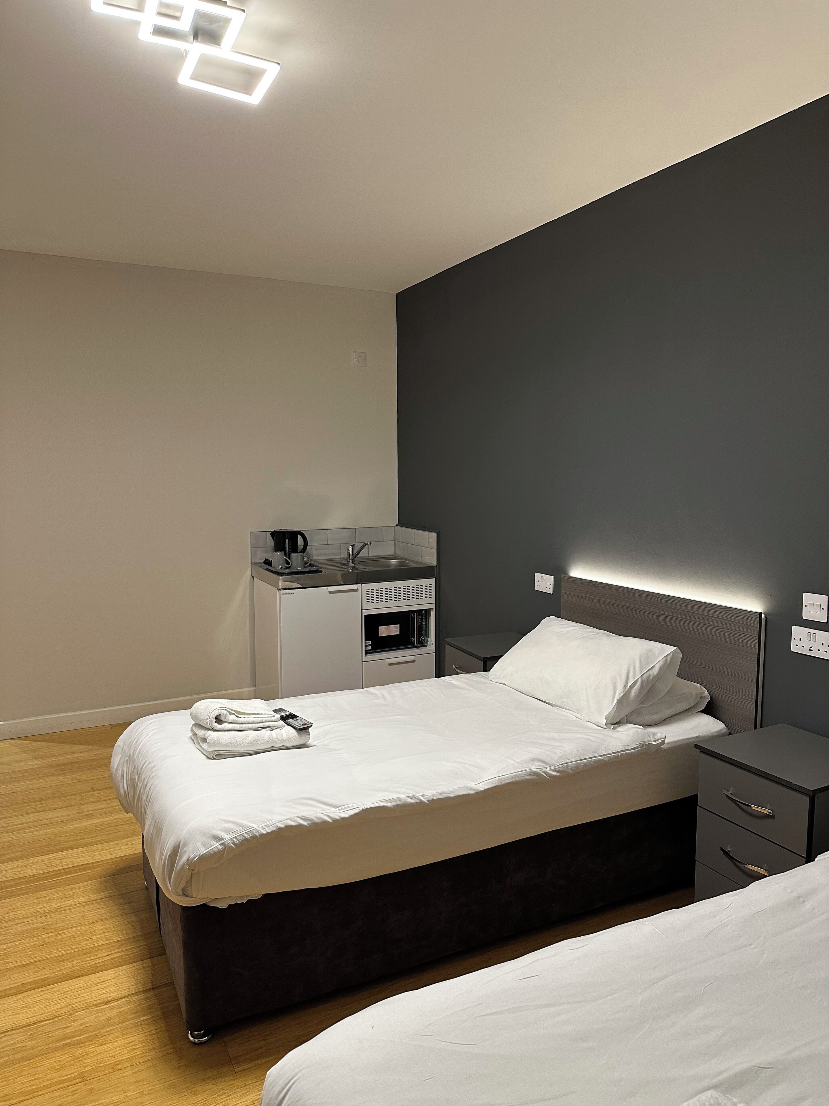 Una camera d'albergo moderna con un letto, un comodino e una scrivania con un bollitore.