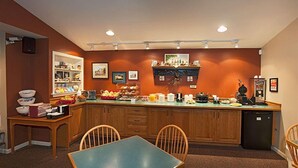 A compact kitchen with wooden cabinets, a dining table, and chairs. There are various kitchen appliances and a refrigerator on the counter. - Travelers Rest Motel (Gordonville)