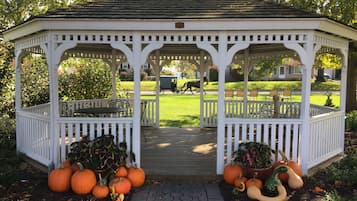 Un kiosque doté d’une terrasse en bois, entouré de plantes en pot et de citrouilles.