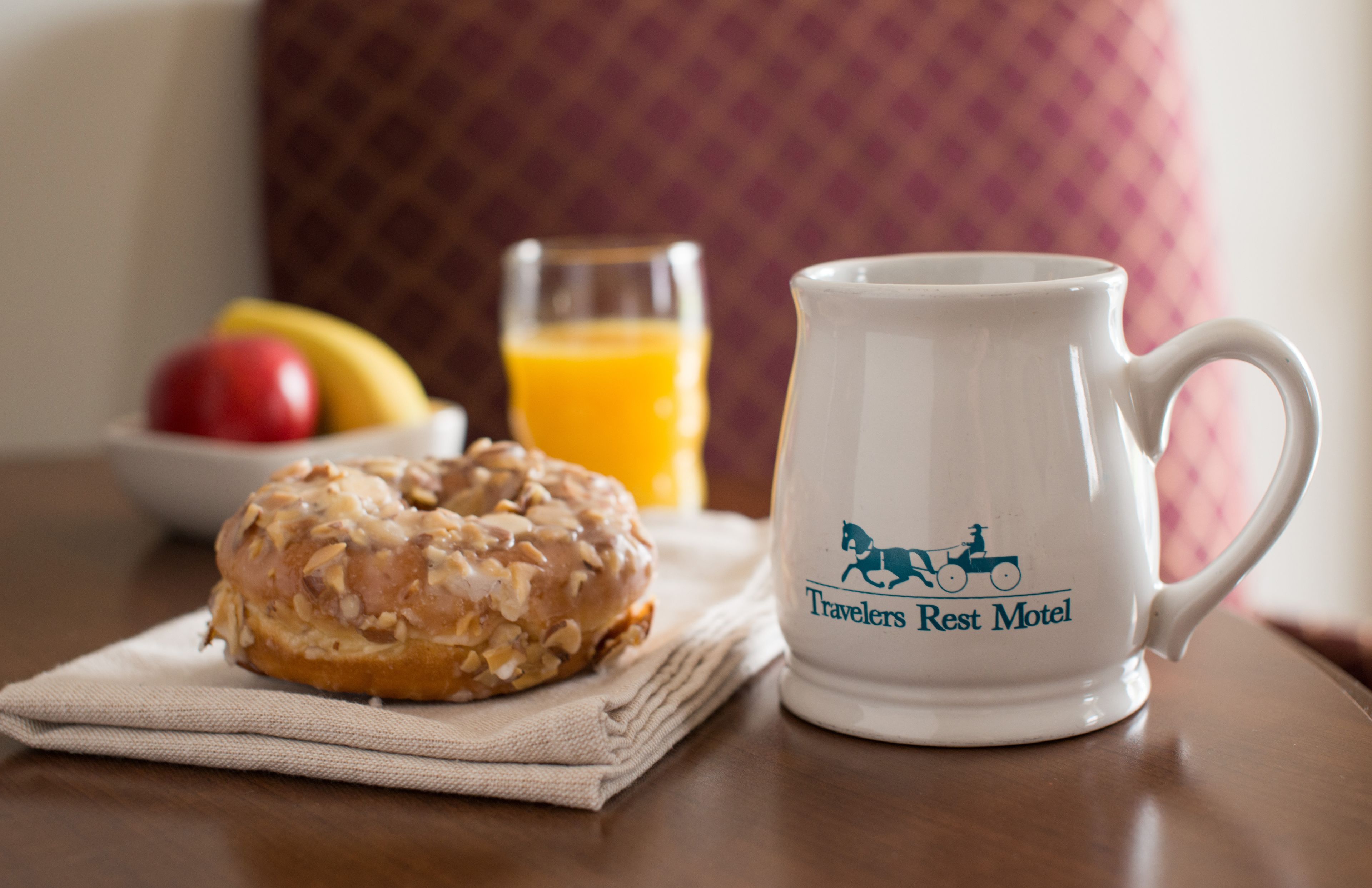 A breakfast setting with a glazed donut, a glass of orange juice, and a mug with a horse logo.