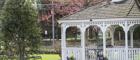 A gazebo with a white roof and columns, surrounded by a garden with potted plants.
