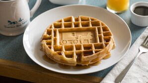 A waffle with syrup on a plate, a coffee cup, a glass of orange juice, and a small bowl of fruit. - Travelers Rest Motel (Gordonville)