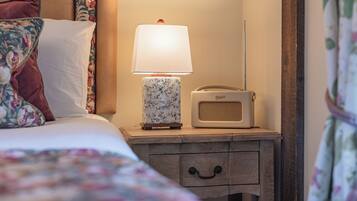 A neatly made bed with floral bedding, a bedside lamp, and a vintage radio on a wooden nightstand.