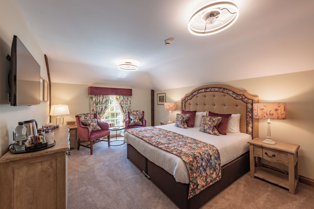 A hotel room with a large bed, a desk with a coffee maker, a chair, and a TV.