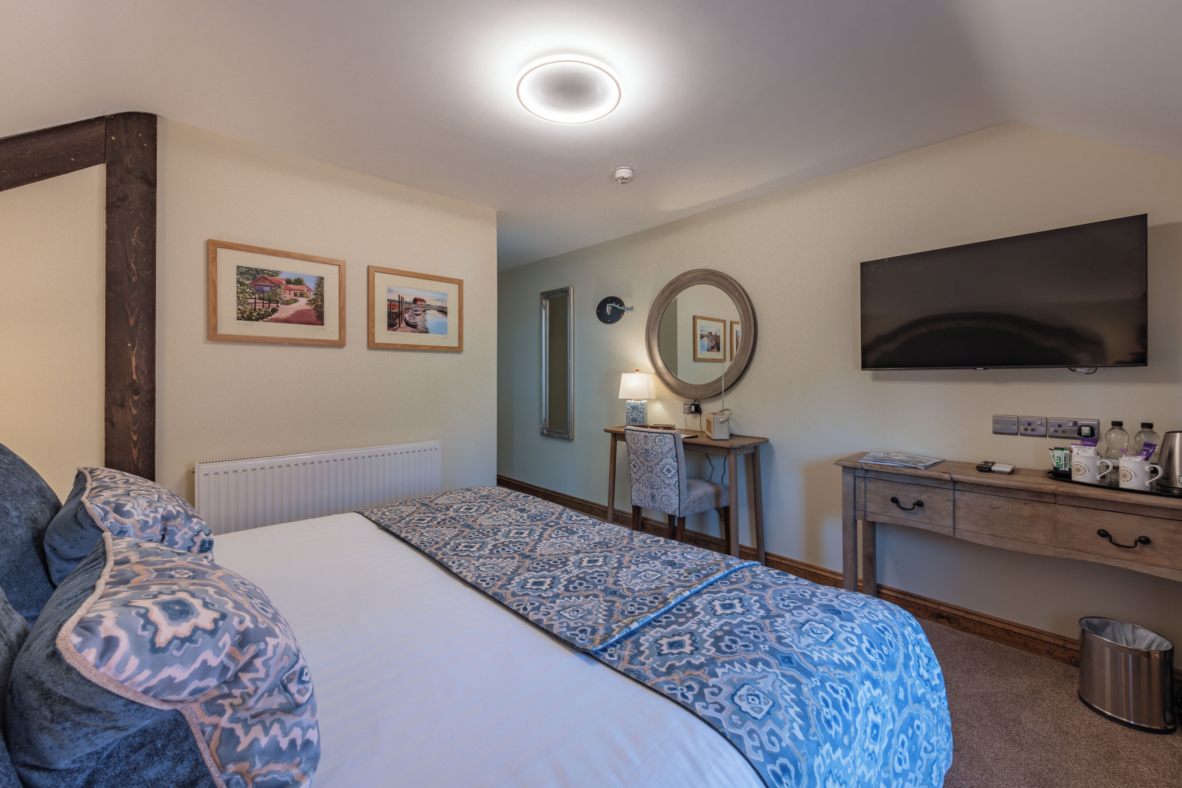 Habitación de hotel con cama, escritorio, televisor y dos cuadros en la pared.