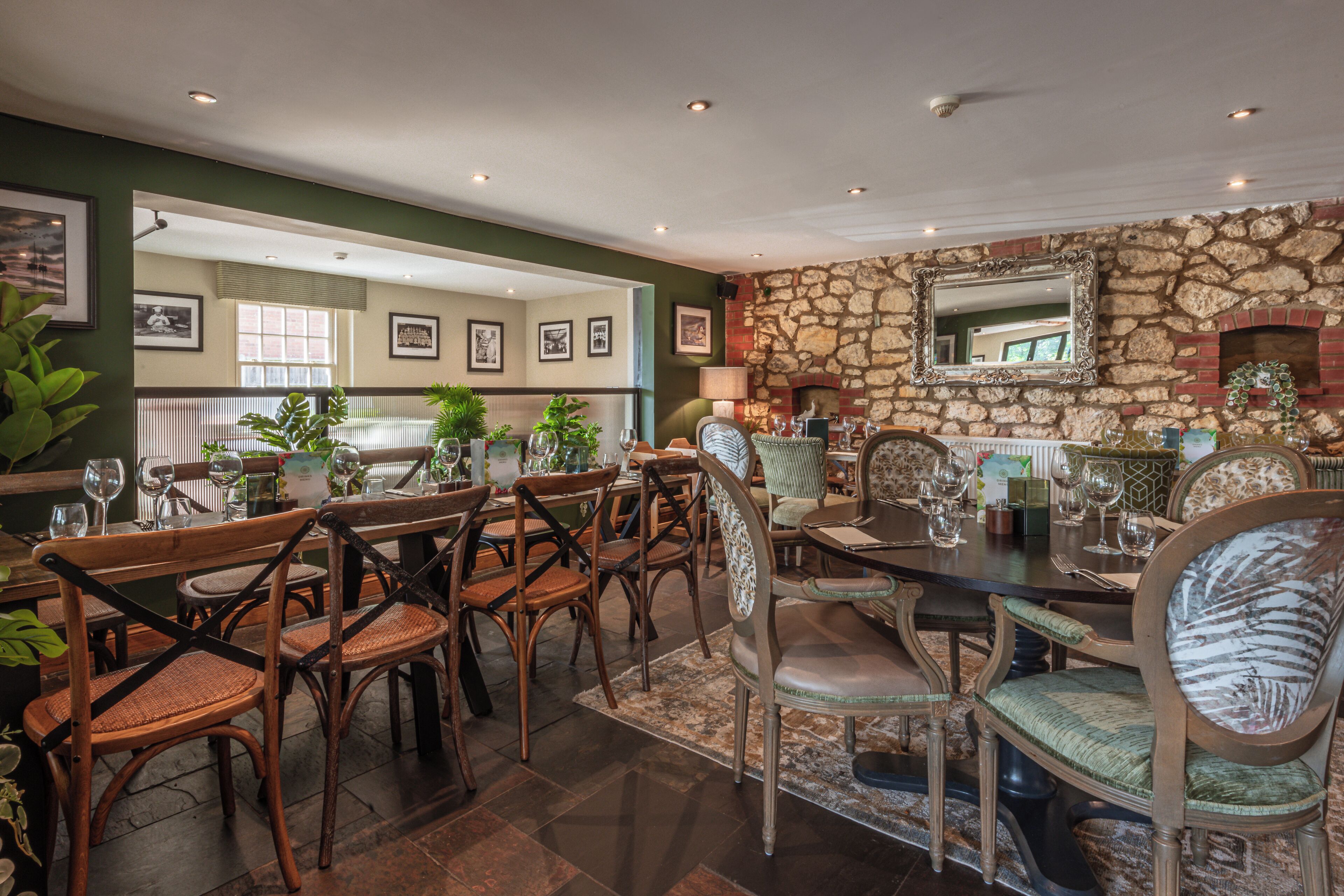 A dining area with wooden chairs and tables, a stone wall, and framed pictures on the wall.