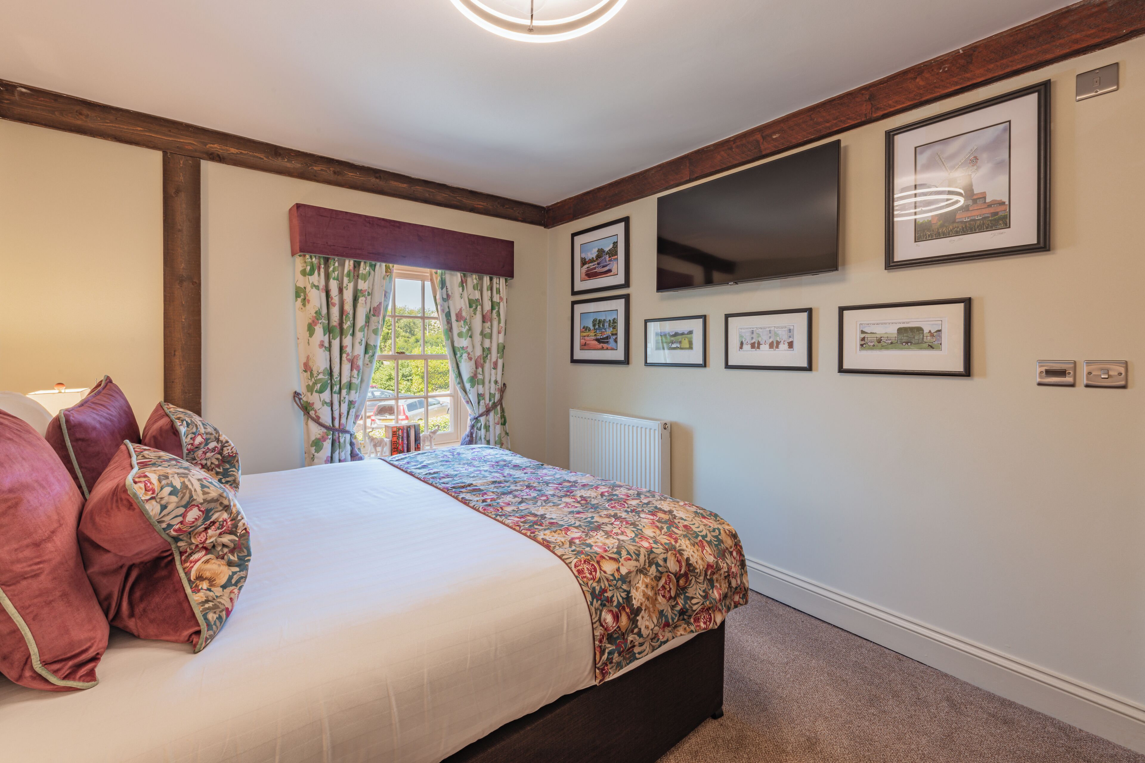 A bedroom with a large bed, floral bedspread, and several framed pictures on the wall.