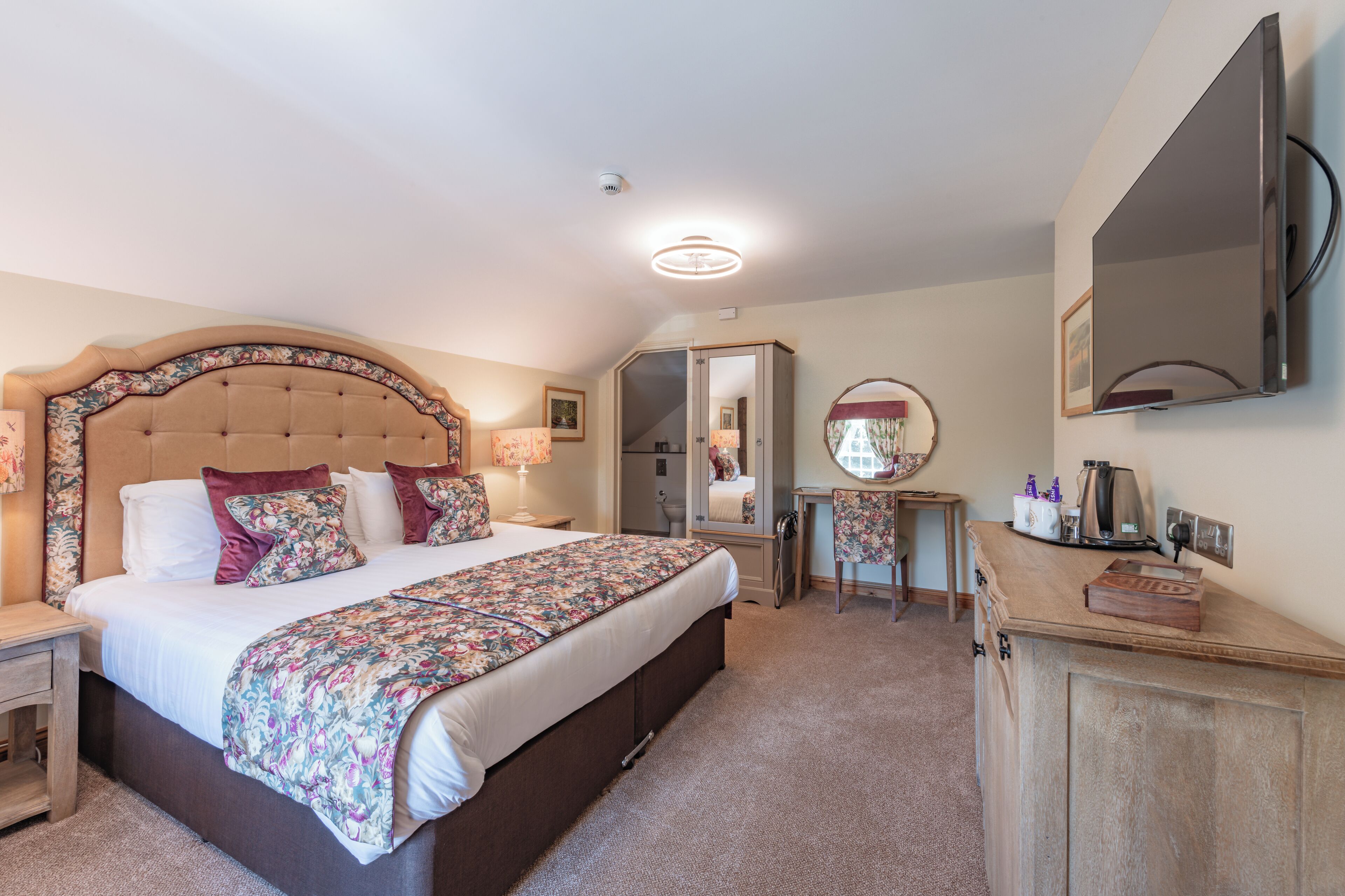 A bedroom with a large bed, a bedside table, a mirror, a dresser, and a ceiling light.