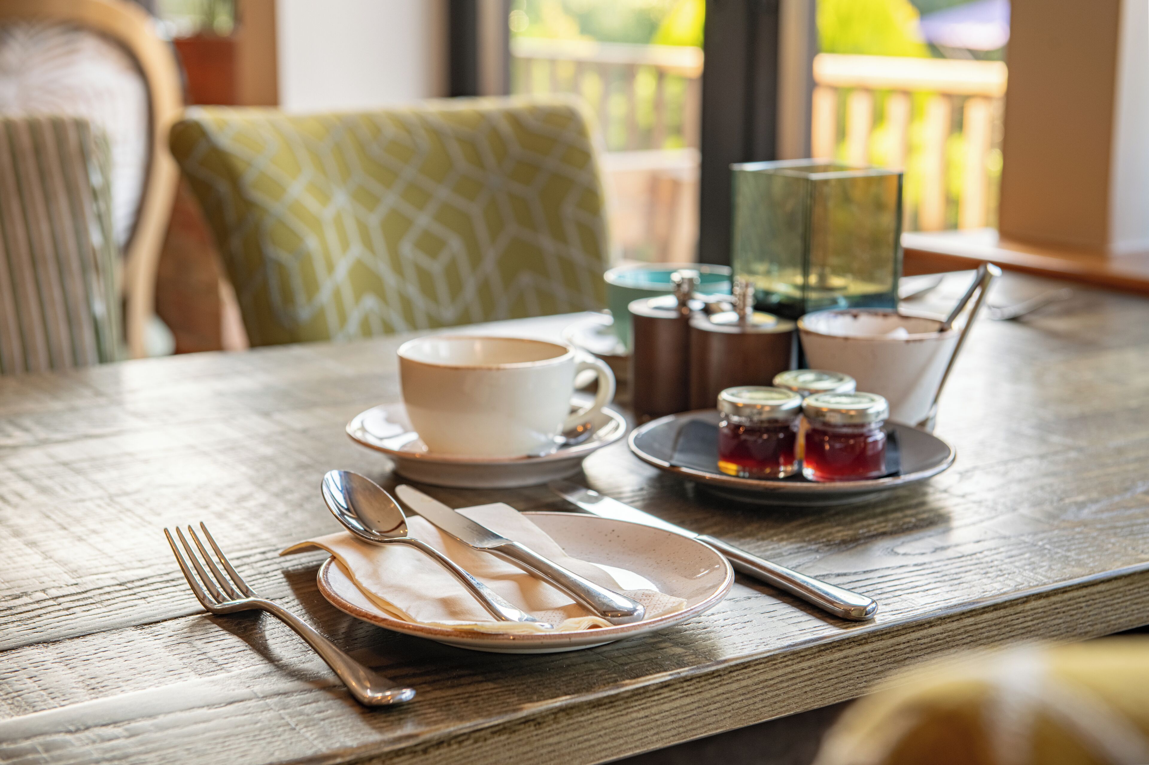 A dining table set with a cup, saucer, plate, cutlery, and condiments.