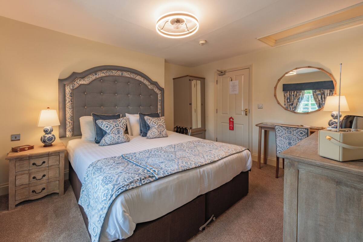 A neatly arranged bedroom with a large bed, bedside tables, a dresser, and a mirror.