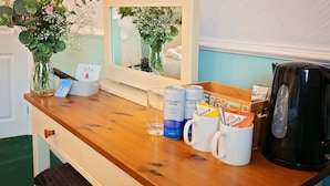Un comptoir en bois avec un miroir, un vase avec des fleurs, une machine à café et une tasse avec une cuillère.