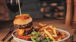 Une assiette comprenant un hamburger, des frites et une salade, accompagnée d’un verre de vin rouge.