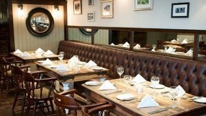 Un restaurant avec des tables en bois et des banquettes en cuir marron, chaque table étant agrémentée de serviettes blanches et de verres à vin.