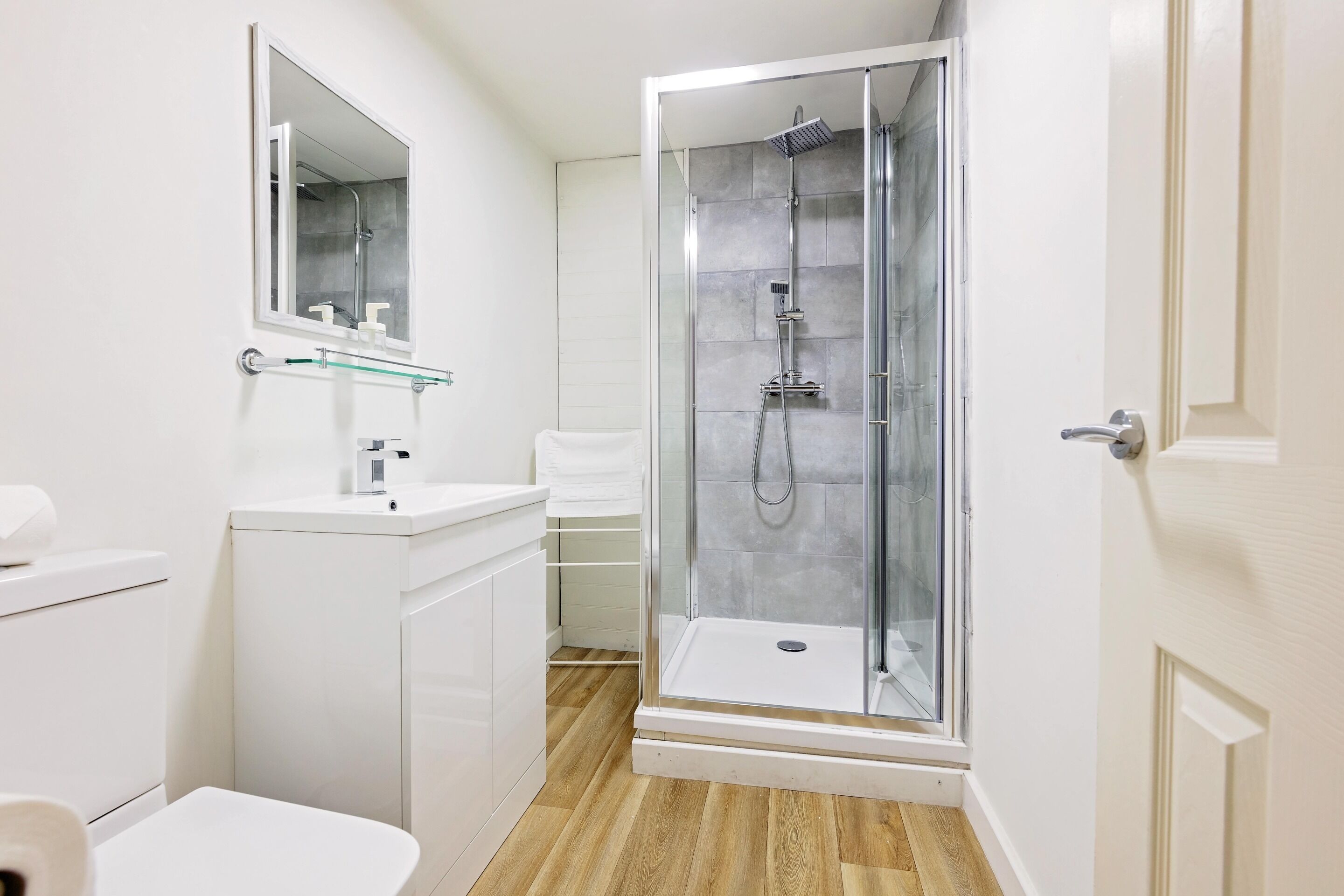 Un baño moderno con ducha acristalada, lavamanos blanco y espejo.