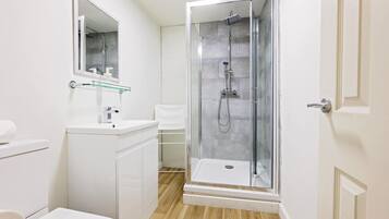 Ein modernes Badezimmer mit einer gläsernen Duschkabine, einem weißen Waschbecken und einem Spiegel.
