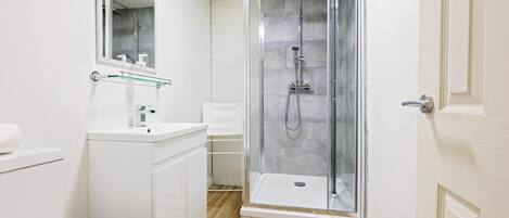Un baño moderno con ducha acristalada, lavamanos blanco y espejo.