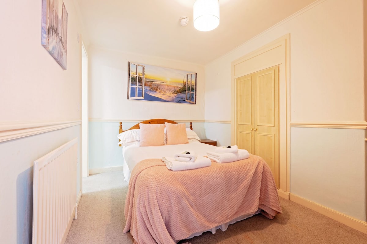 Een slaapkamer met een bed, een schilderij, een radiator en een garderobe.