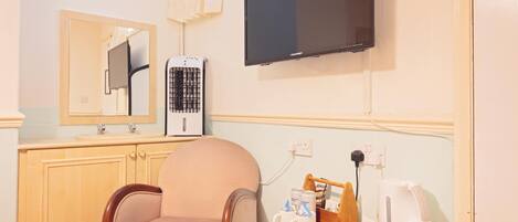 A hotel room with a wooden chair, a small table with a coffee maker, a television, and a heater.