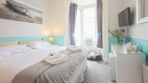 Une chambre d’hôtel avec un lit, un bureau, une télévision et une fenêtre avec des rideaux.