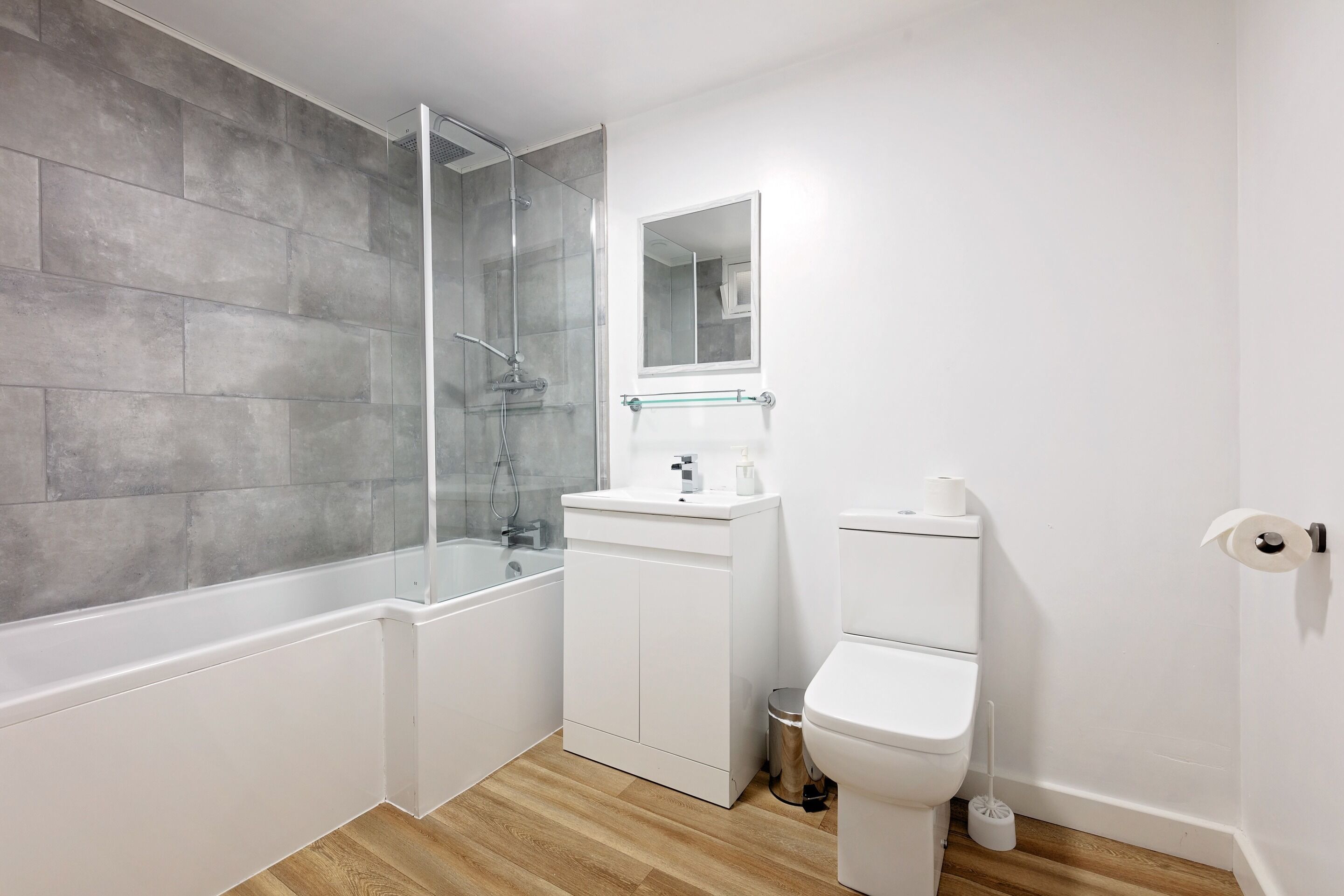 Une salle de bain moderne avec une douche à parois de verre, un lavabo blanc avec un miroir au-dessus et des toilettes.