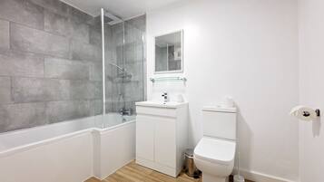 Une salle de bain moderne avec une douche à parois de verre, un lavabo blanc avec un miroir au-dessus et des toilettes.