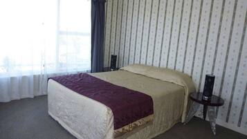 A bedroom with a large bed, a bedside table, a window with curtains, and a patterned wallpaper.