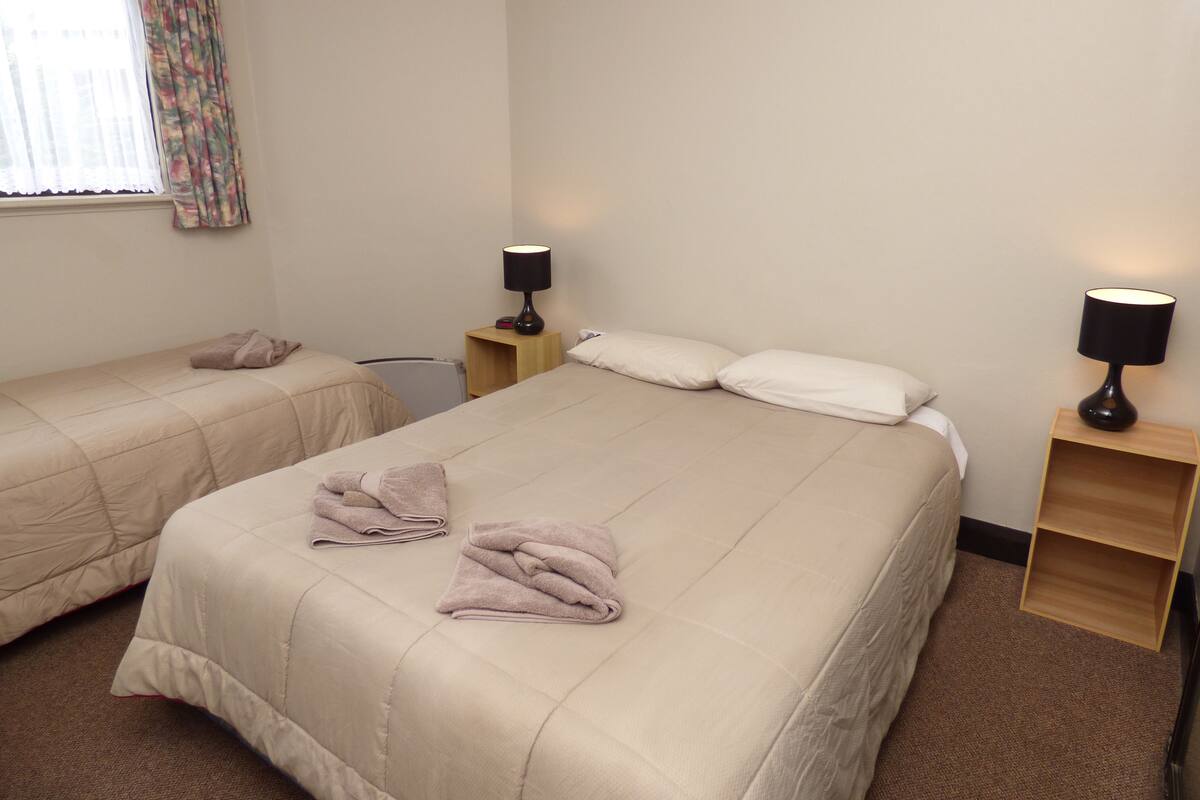 A hotel room with two beds, each with a beige duvet and pillows, and two bedside tables with lamps.