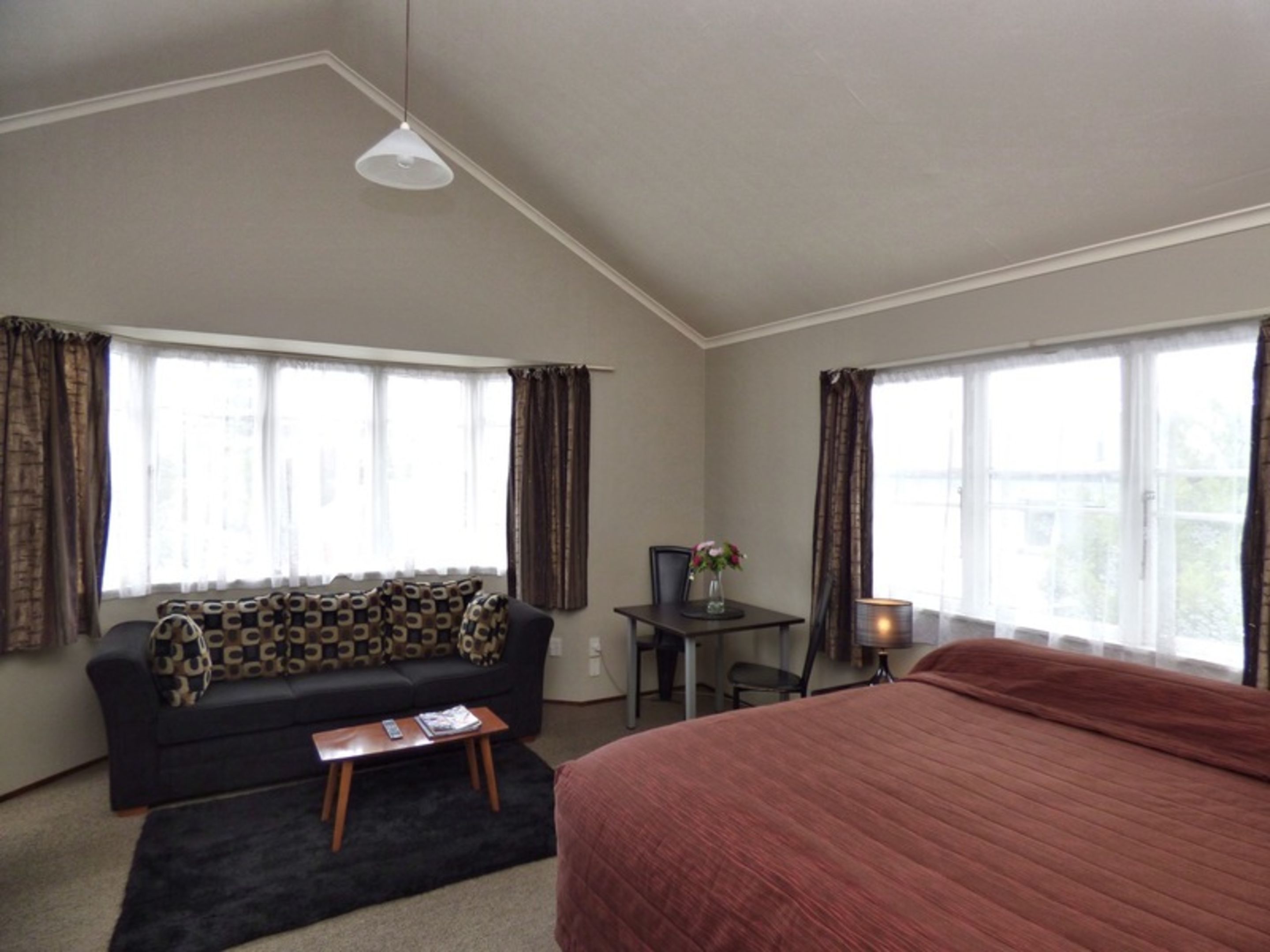 Habitación de hotel con cama, sofá, escritorio y dos ventanas con cortinas.