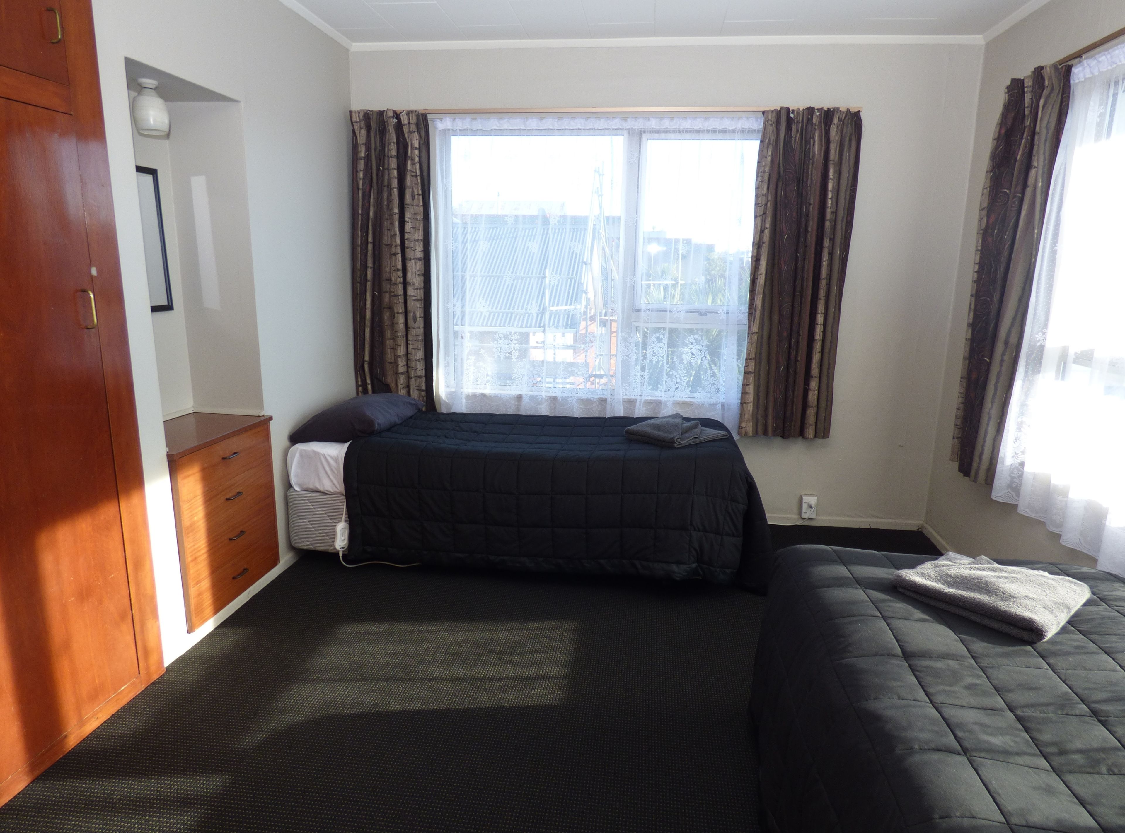 A bedroom with a bed, a dresser, a window with curtains, and a view of buildings outside.