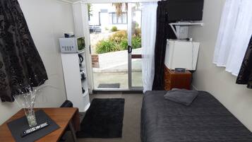 A small, modern room with a bed, a desk with a computer, a TV, and a window with curtains.