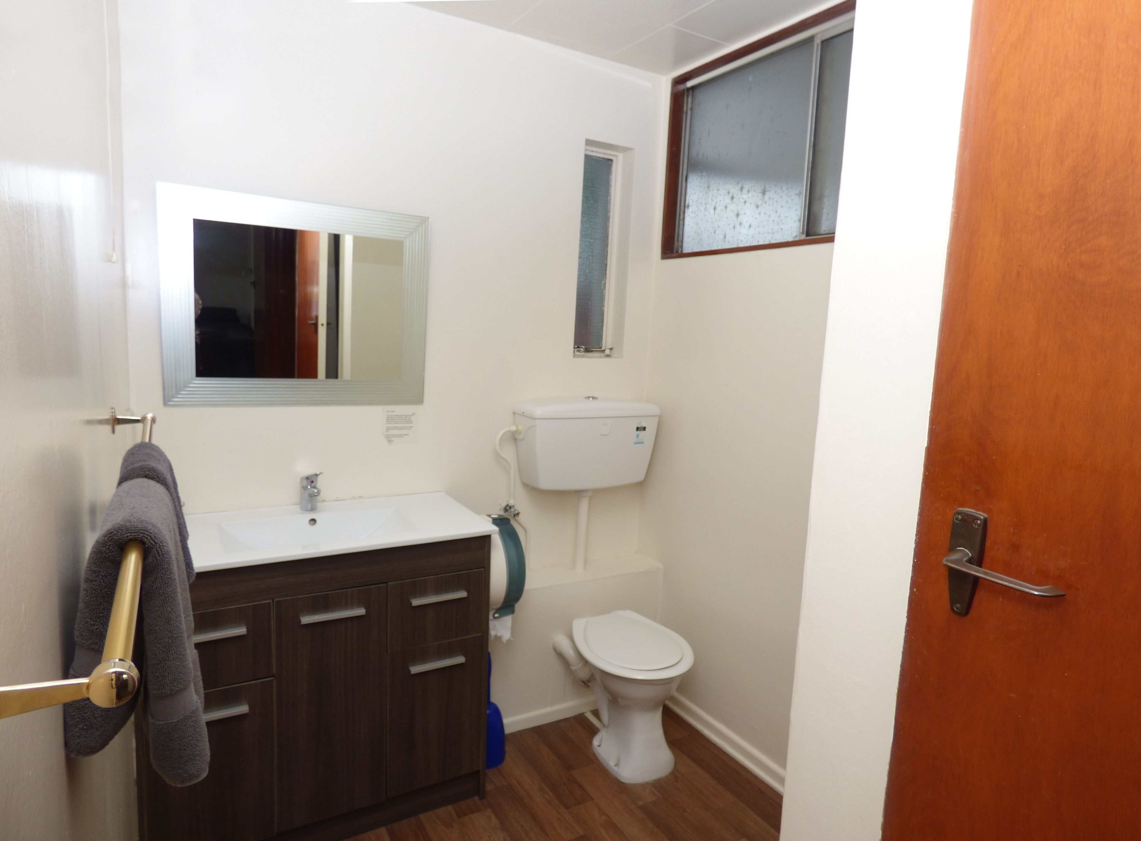 Een compacte, schone badkamer met een witte wastafel, een spiegel, een toilet en een houten deur.