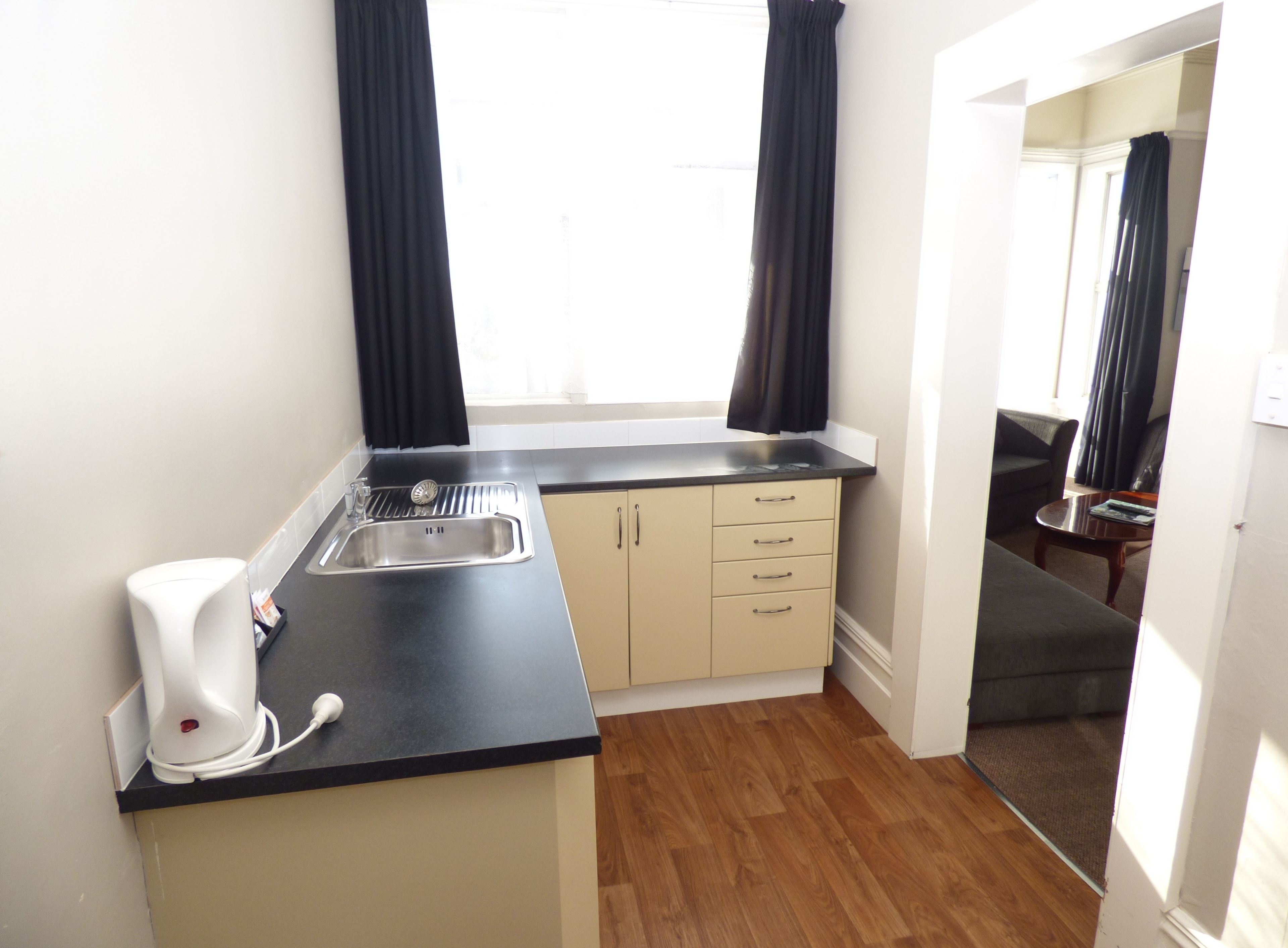 A compact kitchen with a sink, a coffee maker, and a window with curtains.