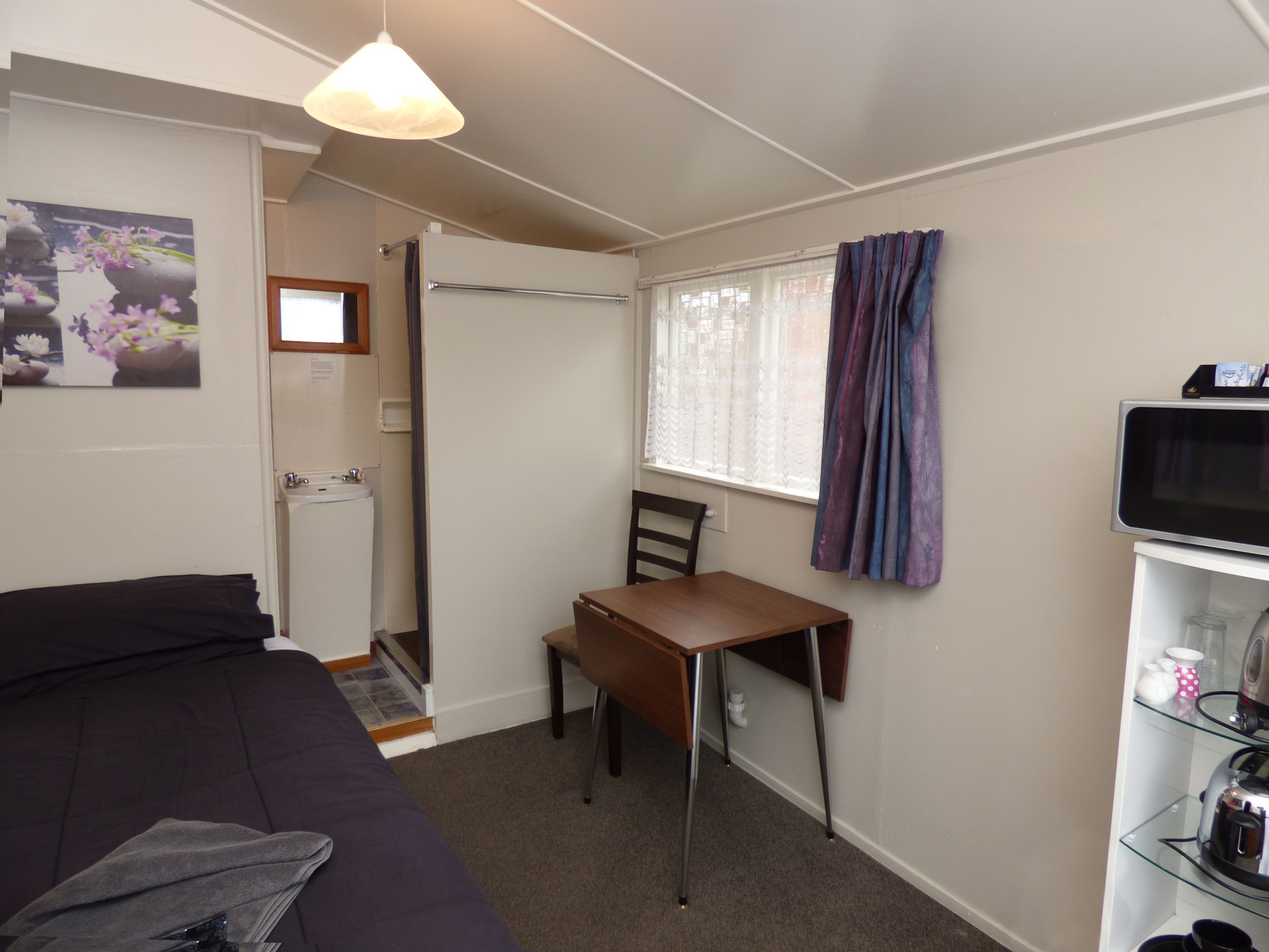 Une pièce de taille modeste comprenant un lit, un bureau, une chaise, un téléviseur et une petite kitchenette.