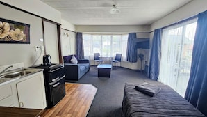 A compact hotel room with a kitchenette, a sofa, a small table, and a TV. - Anchor Motel (Timaru)