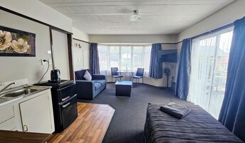 A compact hotel room with a kitchenette, a sofa, a small table, and a TV.