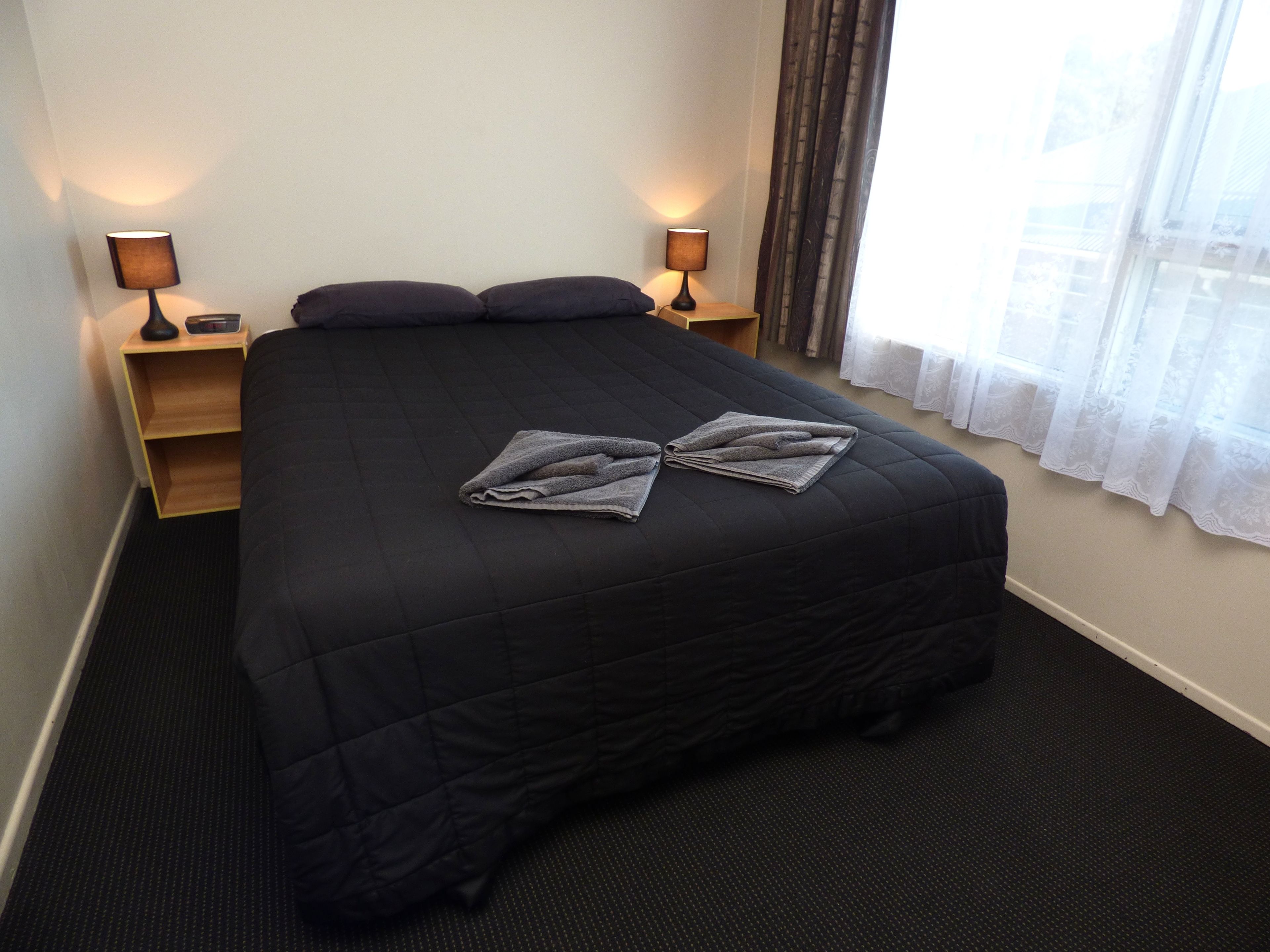 A hotel room with a large bed, two bedside tables, a window with curtains, and a carpeted floor.