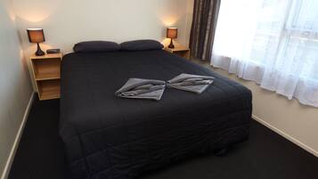 A hotel room with a large bed, two bedside tables, a window with curtains, and a carpeted floor.