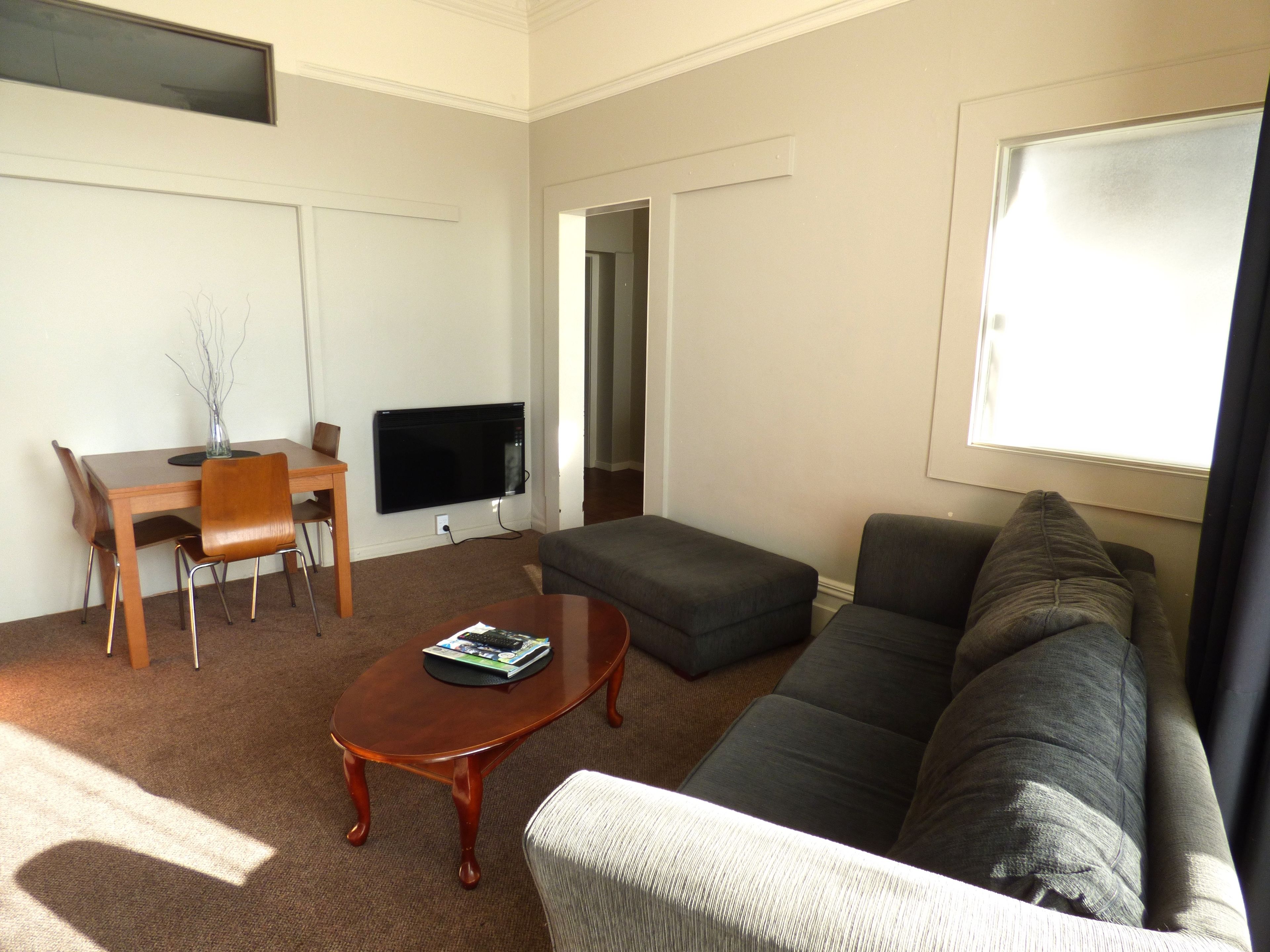 A living room with a sofa, a coffee table, a TV, a dining table with chairs, and a window.